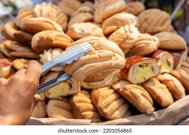 Mexican sweet bread, man taking a loaf of bread from a basket with tongs.