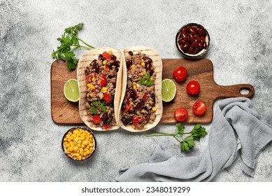 Mexican tacos with beef on a wooden board. Tacos with ground beef, beans, corn and tomato. Gray rustic background. Top view, flat lay.