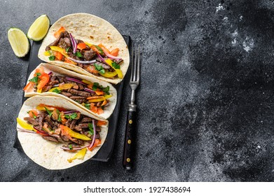 Mexican tacos shells with beef meat, onion, tomato and sweet pepper. Black background. Top view. Copy space.