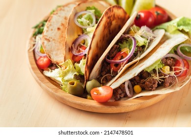 Mexican Tacos In Yellow Corn Tortillas Filled With Carnitas, Onion, Tomatoes And Salad Served In Wooden Plate On The Wooden Background