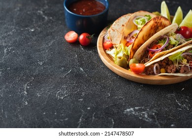 Mexican Tacos In Yellow Corn Tortillas Filled With Carnitas, Onion, Tomatoes And Salad Served In Wooden Plate On The Black Concrete Background