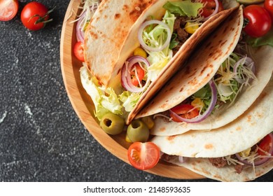 Mexican Tacos In Yellow Corn Tortillas Filled With Carnitas, Onion, Tomatoes And Salad Served In Wooden Plate On The Black Concrete Background