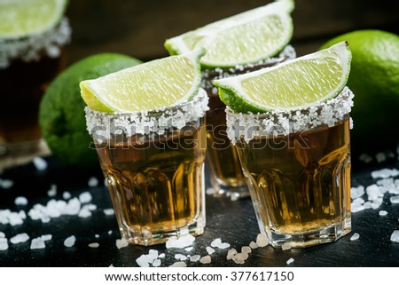 Mexican tequila in a glass, sprinkle with salt with slices of lime on the dark background, selective focus