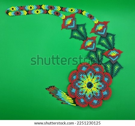 Mexican traditional colorful beads jewelry in curved position on green background. Flowers and leaves, red, purple, green, yellow and turquoise colors