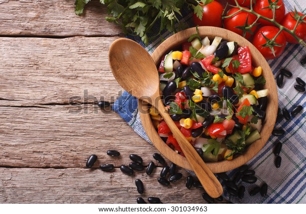Mexican\
vegetable salad with black beans in a wooden bowl, close-up and\
ingredients on the table. Horizontal top\
view\
