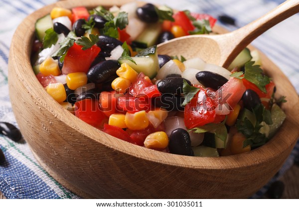 Mexican vegetable salad with\
black beans, avocado and corn close up in a wooden plate.\
horizontal\
