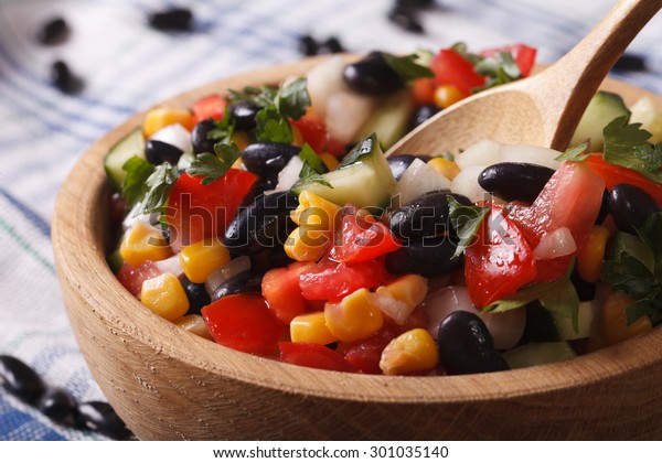 Mexican vegetable salad\
with black beans, avocado, corn and tomatoes macro in a wooden\
plate. horizontal\
