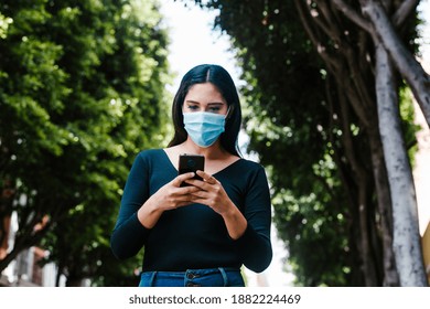 Mexican woman with facemask holding a phone and texting while she is walking in the street of a Latin America city - Powered by Shutterstock