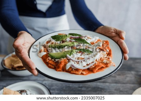 Mexican woman hands preparing chilaquiles with red sauce and eating traditional mexican food for breakfast in Mexico Latin America
