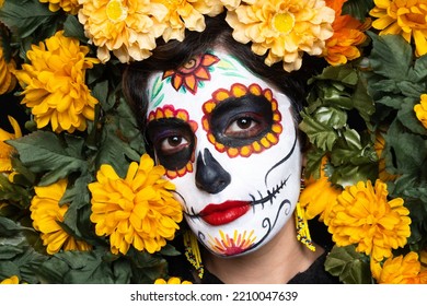 Mexican Woman wears Dia de Los Muertos face paint posed in front of a floral marigold background  - Powered by Shutterstock