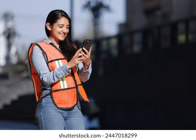 mexican working woman engineer smiling and looking at cell phone with city background - Powered by Shutterstock