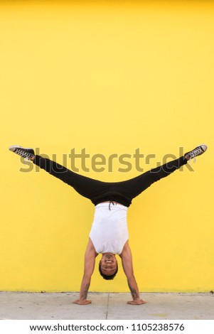 Man practicing yoga, handstand against a yellow wall