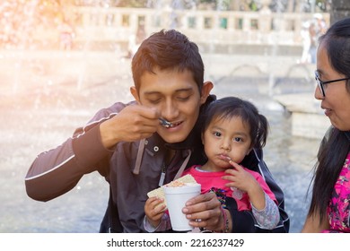 Mexican Young Man Carrying His Little Daughter And Eating Elotes. Hispanic Family. Mexican Food