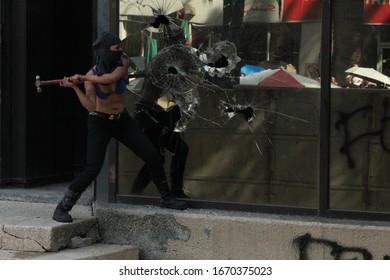 Mexico City, Mexico, 03/08/2020: A Woman With Her Face Covered Is Swinging A Hammer Into A Glass Window, During The Womens´s Day Protest-