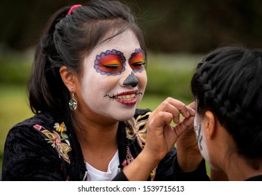 Mexico City / Mexico - November 4, 2018: A Smiling Woman Applies Makeup, Eyelashes And Face Paint To A Girl For Dia De Los Muertos, Or Day Of The Dead In Mexico.