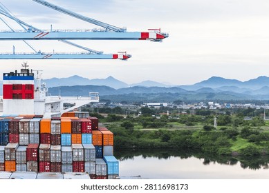 Lázaro Cárdenas, Mexico – Container ship docked at APM Terminals with cargo containers and gantry cranes during sunrise. Aerial view of maritime operations surrounded by mountains and tropical vegetation on the Pacific coast.