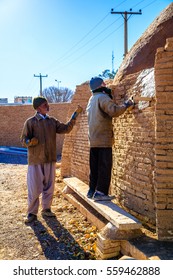 Meybod,Yazd,Iran-December, 11, 2016;skilled craftsman and his helper are cymbals a red mud to the brick wall - Shutterstock ID 559462888
