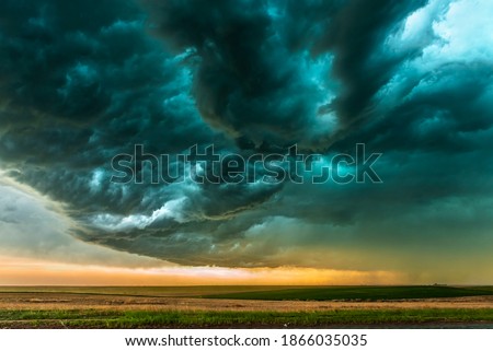 A mezocyclone storm with dark, gray clouds forming over the plains in Tornado Alley, Oklahoma at sunset

