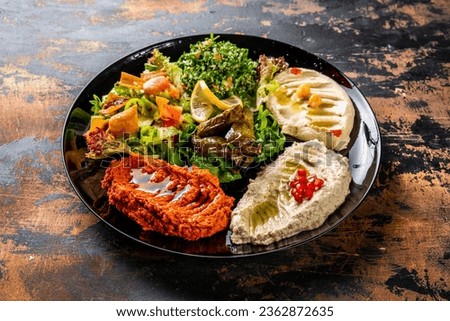 MEZZE PLATTER or mezzeh hummus, vine leaves, tabouleh, baba ganoush, lemon, mutabal served in dish isolated on background top view of arabic food