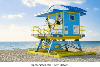 Miami Beach, a couple on the beach in Miami Florida, lifeguard hut Miami Asian women and caucasian men on the beach during sunset. man and woman relaxing at a lifeguard hut looking at a blue ocean - Powered by Shutterstock