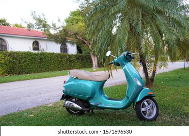 Miami Beach, USA - November 26th, 2019: A Green Vespa Scooter Parked Against A Palm Tree In South Beach, Mediterranean Revival Architecture In The Background. 