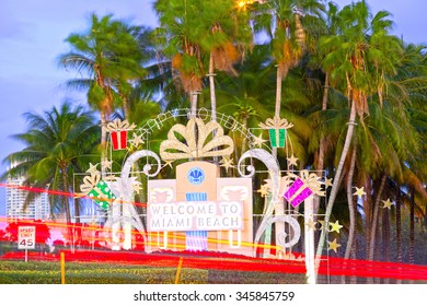 Miami Beach Welcome Sign In Christmas Holiday Decorations And Palm Trees At Sunset With Moving Traffic