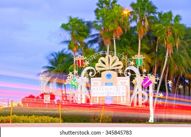 Miami Beach Welcome Sign In Christmas Holiday Decorations And Palm Trees At Sunset With Moving Traffic