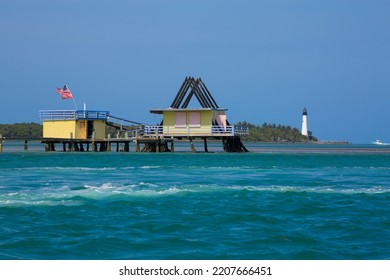 MIAMI, FL - APRIL 2, 2022: Historic Collection Of Homes On Stilts - Known As Stiltsville - In Biscane National Park With Cape Florida Lighthouse And Miami Skyline In The Distance
