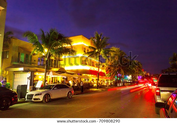 MIAMI, FLORIDA - AUGUST 26, 2017: Cars speed down Ocean\
Drive. The road is the main thoroughfare through South Beach,\
Miami. Ocean Drive scene at night lights, cars and people having\
fun,Miami beach. 