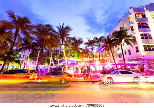 MIAMI, FLORIDA - AUGUST 26, 2017: Cars speed down Ocean\
Drive. The road is the main thoroughfare through South Beach,\
Miami. Ocean Drive scene at night lights, cars and people having\
fun,Miami beach. 