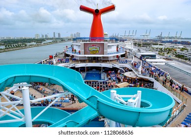 Miami, Florida - March 29 2014: Passengers Onboard The Carnival Liberty Cruise Ship In Miami, On The Top Open Decks With Water Slide And Pool. Miami City Skyline In Background.