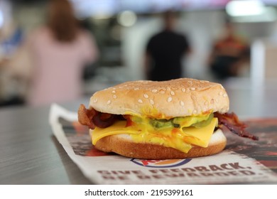 MIAMI, FLORIDA USA - 08-26-2022 
Very Messy Bacon Cheeseburger At A Burger King Restaurant. Some Out Of Focus Restaurant Interior As Backdrop.