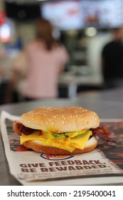 MIAMI, FLORIDA USA - 08-26-2022 
Very Messy Bacon Cheeseburger At A Burger King Restaurant. Some Out Of Focus Restaurant Interior As Backdrop.