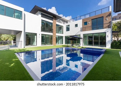 Miami, Florida, USA. January 10, 2020: Garden of a modern mansion in Miami with a swimming pool, artificial grass and some tanning chairs with an umbrella.