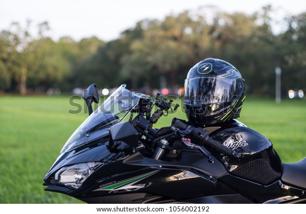 Miami, Florida / USA - October 23, 2017:\
Scorpion full-face modular motorcycle helmet on top of a 2017 black\
Kawasaki Ninja 650 ABS sport bike motorcycle with grass pasture and\
cars in background.
