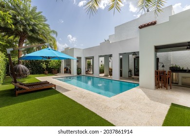 Miami, Florida, USA. September 3, 2021: Backyard of a luxurious house with a swimming pool, artificial grass, grill zone and some tanning chairs with an umbrella.