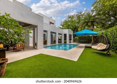 Miami, Florida, USA. September 3, 2021: Backyard of a modern house with swimming pool, artificial grass, trees, chairs and an umbrella.