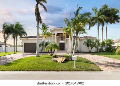 Miami, Florida, USA. September 9, 2020: Facade of the entrance to a mansion with wooden doors, garage, palm trees, grass and a blue sky.