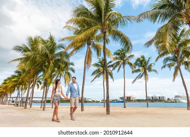Miami people lifestyle - couple walking holding hands talking enjoying walk on beach with palm trees. Florida travel destination.