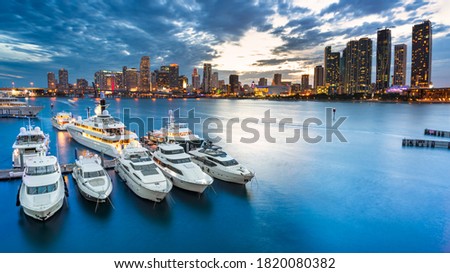 Miami skyline at dusk on cloudy evening with dramatic sky showing brickell and downtown and the marina in the foreground with the large impressive yachts and boats 