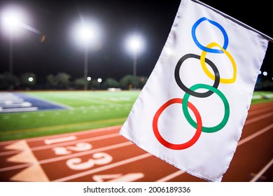 MIAMI, USA - AUGUST 15, 2019: An Olympic flag waves under the floodlights of a red athletics track.