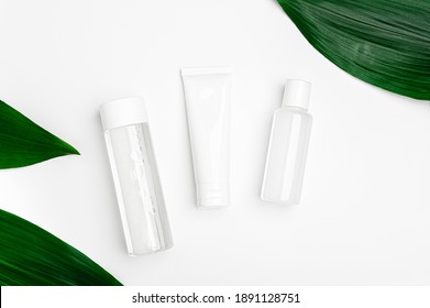 Micellar water, cream and lotion in a transparent package on white background with green leaves. Cosmetic natural organic bio products top view. Set of beauty products for face, body and hand skincare