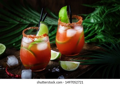 Michelada - Mexican alcoholic cocktail with beer, lime juice, tomato juice, spicy sauce and spices, vintage wooden background, selective focus