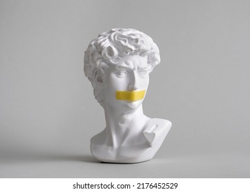 Michelangelo's David head bust in duct tape sealed mouth. Minimal concept on gray background censorship of freedom of speech and restrictions of thought and word. Fight for your rights.