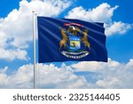Michigan flag waving in the wind on clouds sky. High quality fabric. International relations concept
