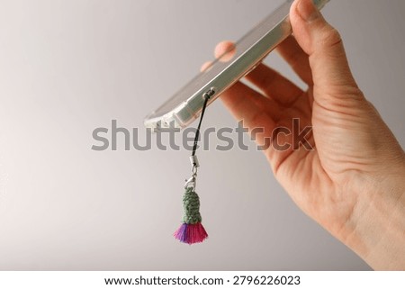 Micro knitting phone accessory strap with purple pink blossom trinket on mobile device cover for electronic shop fashion boutique souvenir store ecommerce catalog promotion webpage