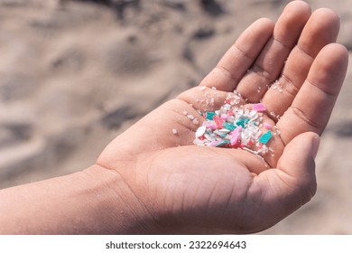 Micro plastics or Microplastics found on the beach on a person's hand on Mexico, sea sand in the background.