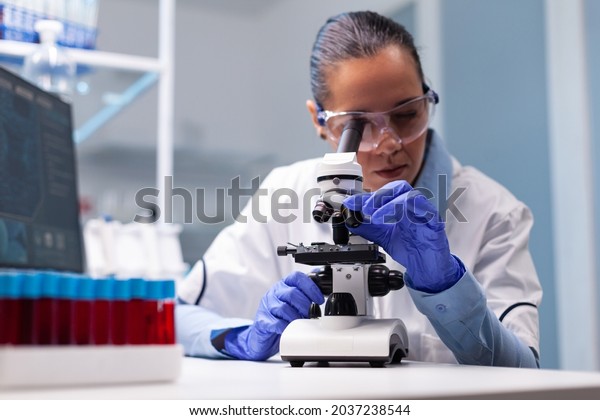 Microbiologist doctor woman analyzing vaccine\
results using medical microscope researching bacteriology infection\
diagnostics against coronavirus. Specialist doctor working in\
biotechnology\
laboratory