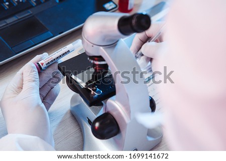 Microbiologist making notes after coronavirus test. Analysis of test tube with a sample. Tube of biological sample contaminated by Coronavirus. Positive results. Medical exam. Epidemiology. Pandemic.