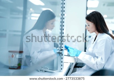 A microbiologist performs aseptic techniques in a laminar flow hood. She is processing a biological sample for pharmaceutical research and drug development.